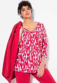 Rood-wit gestreepte top met een V-hals en driekwartmouwen, gecombineerd met een bijpassende rode blazer en broek.