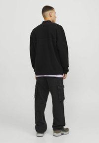 Black fleece jacket with a high collar over a light purple shirt, paired with dark cargo pants featuring large pockets, and gray sneakers.