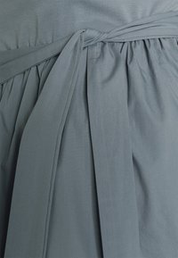 Tela de vestido gris claro con pliegues recogidos y un lazo en la cintura. Textura suave y acabado liso. Diseño minimalista sin patrones visibles.