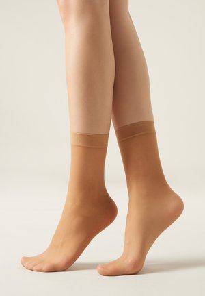 Calcetines tobilleros beige con una textura suave y puños elásticos, diseñados para ajustarse cómodamente, mostrando un aspecto de tono de piel natural.
