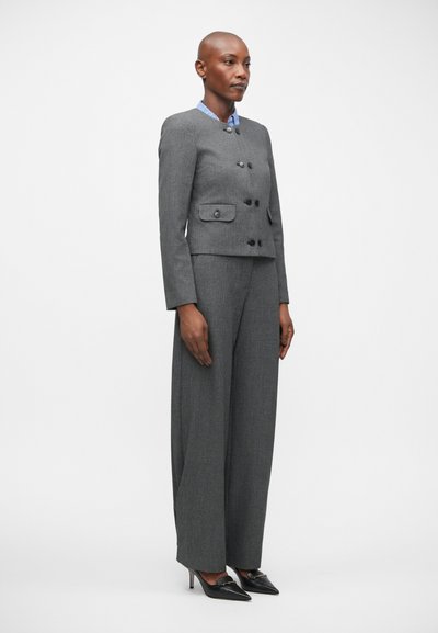 Grijze op maat gemaakte kostuum met een getailleerde blazer en wijduitlopende broek, gecombineerd met een blauw gestreept overhemd met kraag. Zwarte hakken maken de look compleet.