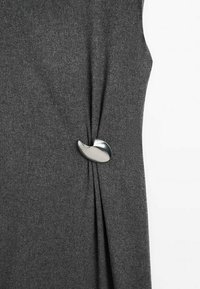 Grau gestricktes Kleidungsstück mit einer glatten, silbernen, geschwungenen Knopfdetaillierung, versehen mit drapierten Falten und einer strukturierten Stoffoberfläche.