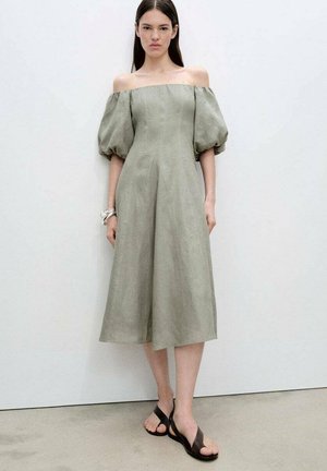 Oliviavihreä off-the-shoulder-mekko, jossa on puffihihat, polvipituinen, kevyestä kankaasta valmistettu, yhdistettynä ruskeisiin sandaaleihin.