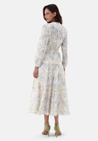 Blumenkleid im Maxistil aus leichtem Material, mit tailliertem Schnitt, langen Ärmeln und gestuften Saum. Farben sind Weiß, Gelb und Grau.