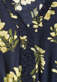 Tissu bleu foncé avec motifs de fleurs jaunes et feuilles vertes présentant un détail d'encolure en V froncée et plissée.