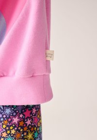 Roza jopa z rebrastimi manšetami, na kateri je bleščeč grafični motiv. Kombinirana z legicami, ki imajo večbarven vzorec zvezd na temnem ozadju.