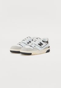 Sapatilhas desportivas brancas e cinzas com um cabedal em camurça e malha, detalhes pretos, sola de borracha cinza e um colarinho almofadado para conforto.