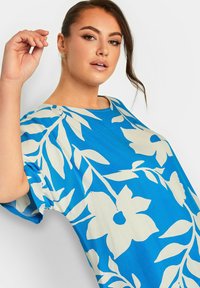 Top blu con stampa floreale caratterizzato da scollatura rotonda e maniche corte. Realizzato in tessuto leggero con grandi motivi di fiori e foglie bianchi.