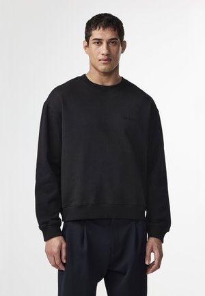 Black crewneck sweatshirt made of textured fabric, featuring a subtle logo on the chest, and a relaxed fit with ribbed cuffs and hem.