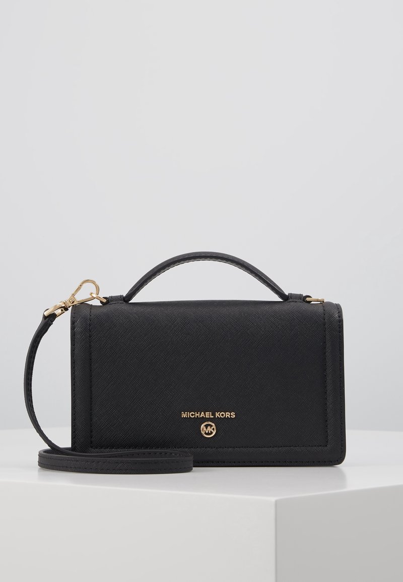 Sac à main Michael Kors noir avec logo doré, poignée supérieure et bandoulière amovible sur une surface blanche avec un fond uni.