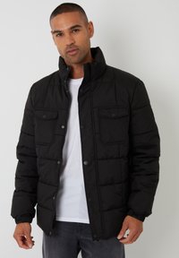 Schwarze Pufferjacke mit hohem Kragen, vorderem Druckknopf- und Reißverschluss, zwei Brusttaschen, gesteppten Panels und strukturiertem Stoff.