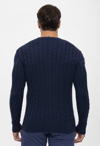 Tumedast kaelustega nööri kudumise kampsun, millel on tekstuurilised mustrid, pikad varrukad ning ribagiha ja alläärega. Tagantvaade näitab keha külge kõvale sobivat disaini.