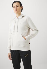 Sweatshirt à capuche beige clair avec poche kangourou, cordons de serrage et logo Nike subtil. Le matériau semble doux avec des poignets et un ourlet côtelés.
