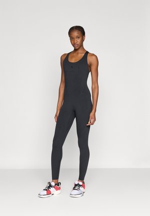 Body deportivo negro con escote redondo y espalda estilo racerback. Presenta detalles perforados y un diseño ajustado. Se lleva con zapatillas deportivas coloridas.