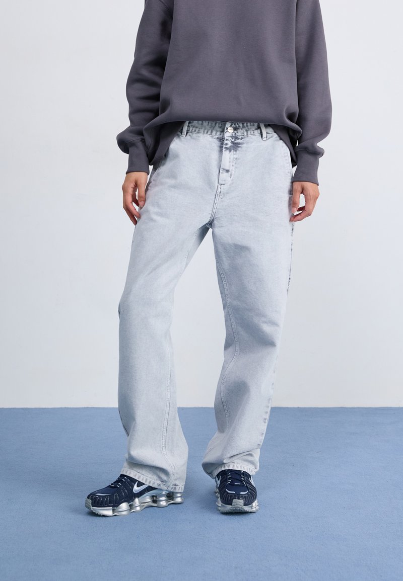Lichtgrijze denim jeans met een ontspannen pasvorm, voorzien van een hoge taille en zijzakken, gecombineerd met donkere sportieve sneakers en een grijze sweatshirt.