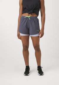 Grå atletiske shorts med en lyseblå innside, med elastisk linning og grønt snor, kombinert med svarte sneakers.