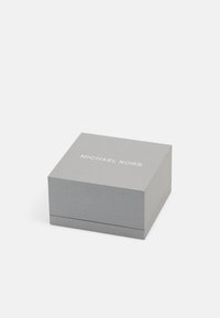 Harmaa suorakulmainen laatikko, jossa on teksturoitu pinta, ja jonka päällä on valkoinen "Michael Kors" -logo. Suunniteltu asusteiden pakkaamiseen.