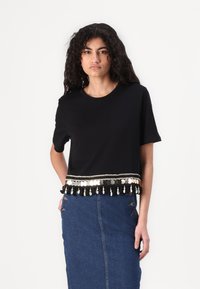 Camiseta corta negra con un borde decorativo que presenta adornos plateados y negros. Combinada con una falda de mezclilla azul.