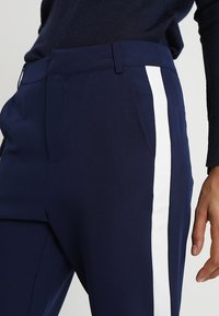 Marinblå skräddarsydda byxor med en mjuk textur, med vita sidostråk, rak passform och en synlig framficka.