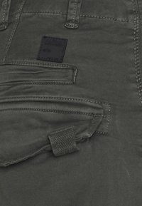 Spodnie cargo w kolorze antracytowym wykonane z trwałej tkaniny, z kwadratową czarną metką, licznymi kieszeniami oraz kontrastowymi przeszyciami.