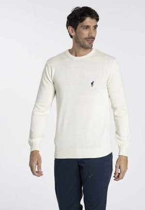 Pull en tricot couleur crème avec un col rond, des poignets et un ourlet côtelés, arborant un petit logo de cheval marine sur la poitrine.