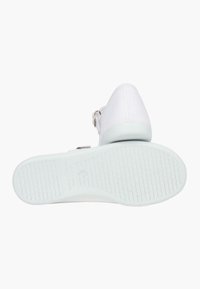 Zapato blanco tipo slip-on con una parte superior de lona suave y una suela de goma texturizada en color verde menta. Presenta una hebilla plateada y un diseño minimalista.