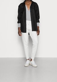 Camicia nera con bottoni sopra un maglione grigio a collo a V e pantaloni bianchi da jogging, accentuata da sneakers bianche. Design semplice e texture morbide.