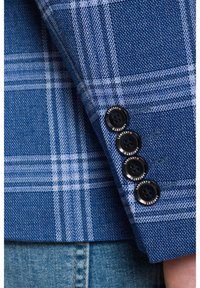 Niebieska kraciasta rękaw kurtki z teksturowanej tkaniny oraz czterema czarnymi guzikami z logo "Lancerto" na mankiecie.