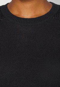 Svart stickad tröja som har ett texturerat tyg, ribbad halsringning och en åtsittande design som framhäver dess vävda detaljer.