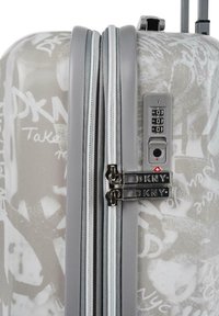 Maleta rígida en gris con patrones abstractos en blanco. Presenta cremalleras dobles, la marca DKNY y un candado de combinación. Textura suave.