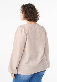 Dlhý rukáv, svetloružový top s vzorom a balónovými rukávmi, s okrúhlym výstrihom, v kombinácii s modrými džínsovými nohavicami. Mäkka textúra látky.