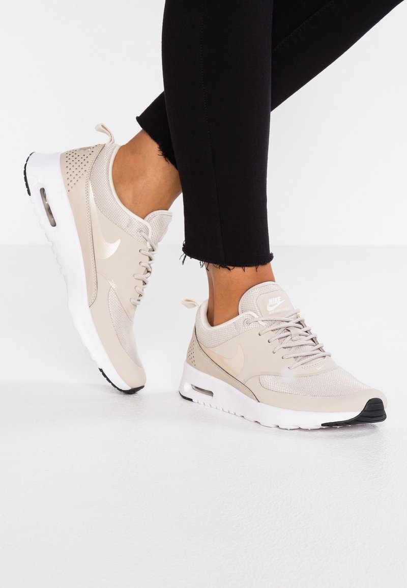 Béžové tenisky Nike s horní částí z mesh materiálu, čern ými akcenty a bílou podrážkou. Jsou zdobeny perforacemi a mají ploché tkaničky.