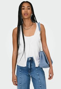 Top bianco senza maniche con scollatura a V e dettagli con bottoni, abbinato a jeans blu a vita alta e una morbida borsa blu.
