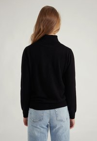 Maglione nero a maglia con collo alto e maniche lunghe, abbinato a jeans azzurri chiari a vita alta con tasche posteriori.