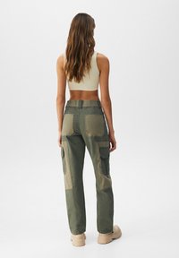 Zelené cargo kalhoty vyrobené z bavlněné směsi, s akcenty z nášivek, bočními kapsami a volným střihem. Zobrazená zadní část je zkrácená.