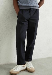 Tumesed sirge lõikega püksid, millel on küljetaskud ja sile tekstuur, koos valgete tossudega ja halli mustriga topp.