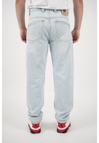Vaqueros de mezclilla azul claro con corte recto, bolsillos traseros y una etiqueta de cuero en la cinturilla; combinados con zapatillas rojas y blancas.