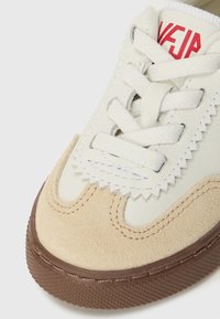 Hvite lær sneakers med beige suedepaneler, rund tå, flate lisser, taggete detaljer og en brun gummisåle. Rødt merke logo på tungen.