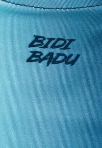 Tessuto blu chiaro con una superficie testurizzata; presenta la scritta nera "BTDI BADU" in un font stilizzato vicino al bordo superiore.