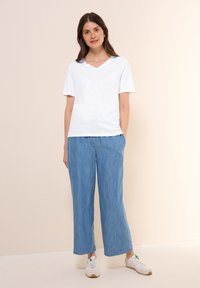 Hvid V-hals t-shirt parret med lyseblå brede bukser, der har en afslappet pasform og blødt stof, båret med hvide sneakers.