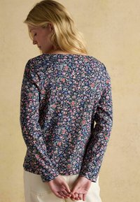Kvetinový top s dlhým rukávom v námorníckej modrej farbe s ružovými a zelenými vzormi, okrúhly výstrih a priliehavý strih, na modeli otočenom chrbtom.