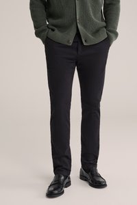 Černé kalhoty z látky s úzkým střihem, hladkou texturou a klasickým designem, doplněné lesklými černými mokasíny.