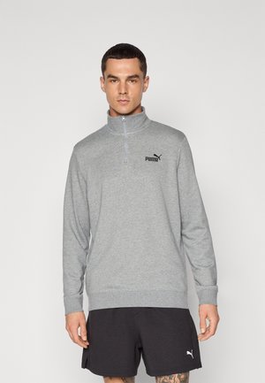 Grå quarter-zip pullover i blødt materiale med lange ærmer, ribbede mansjetter og et sort Puma-logo på brystet. Sammen med sorte shorts.