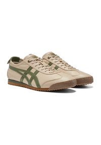 Beige leather sneakers with green accents, textured rubber outsole, and flat laces. Features a low profile and rear pull tab.