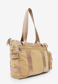 Beżowa torba tote wykonana z tkaniny, z zamykanymi kieszeniami, beżowo-białymi akcentami, regulowanym paskiem na ramię oraz teksturą w kratkę.