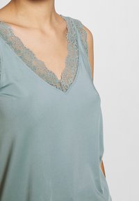 Light blue sleeveless top featuring a V-neck with delicate lace trim, smooth fabric, and relaxed fit. Lace has floral pattern detailing.