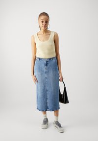 Kootud kreemjas top, millel on lainelised servad, kombineeritud keskmise sinise denimpikkseelikuga, hallide tennisetossudega ja musta käekotiga.