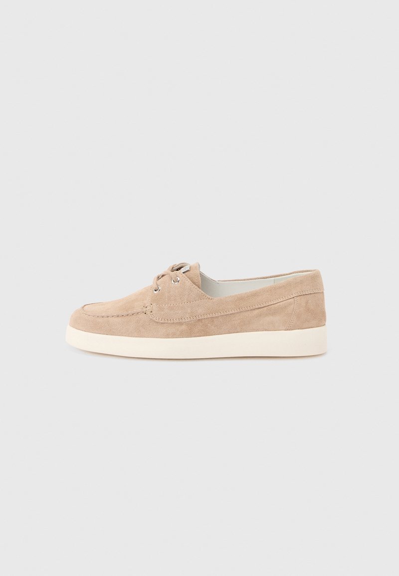 Chaussure décontractée beige en daim à lacets avec semelle en caoutchouc blanche, vue de profil sur un fond gris clair uni.
