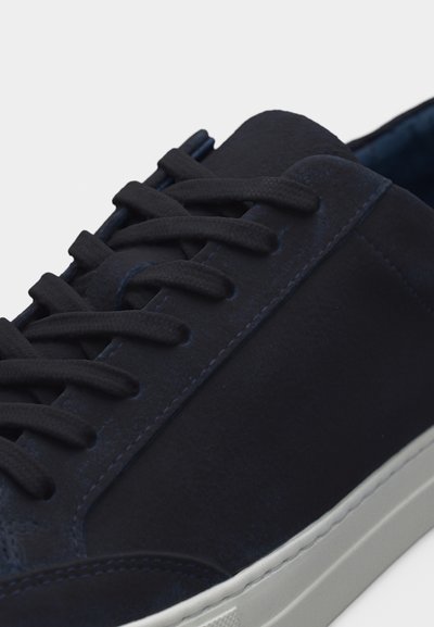 Σκούρο μπλε σουέντ αθλητικό παπούτσι με κορδόνια στο ίδιο χρώμα και λαστιχένια λευκή σόλα, εμφανίζοντας κοντινή λήψη του επάνω μέρους και των λεπτομερειών της ραφής.