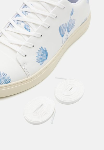 Hvit sneaker med blå blomstertrykk, flate hvite lisser, teksturert overdel og en kremfarget såle. To ekstra hvite lisser inkludert.